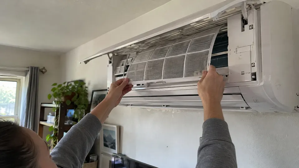 Hands sliding a clean dry filter back into an open wall mounted mini split