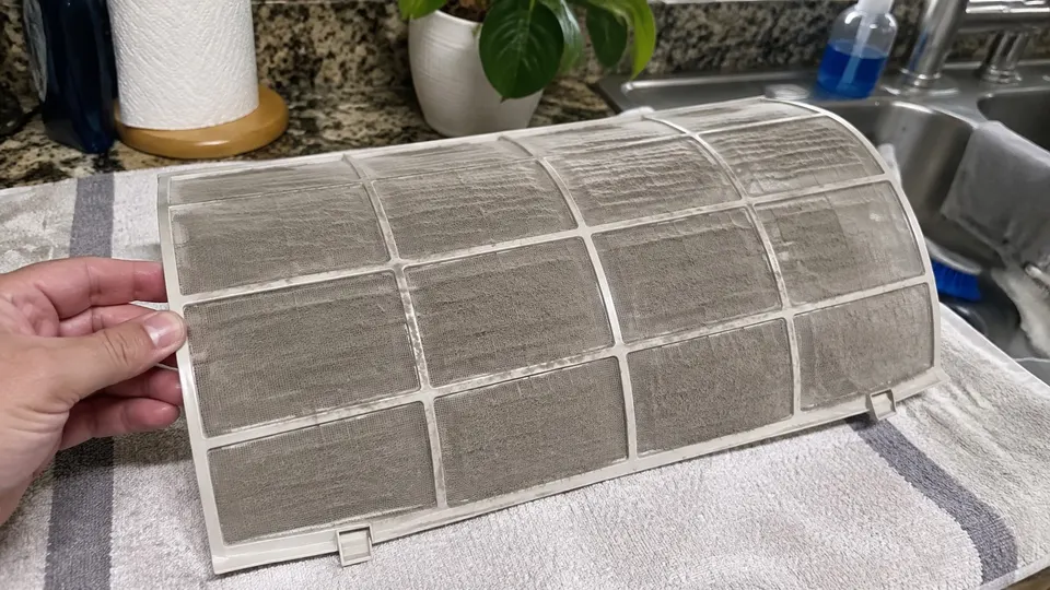 Mini split mesh filter lying on a towel with a visible layer of gray dust